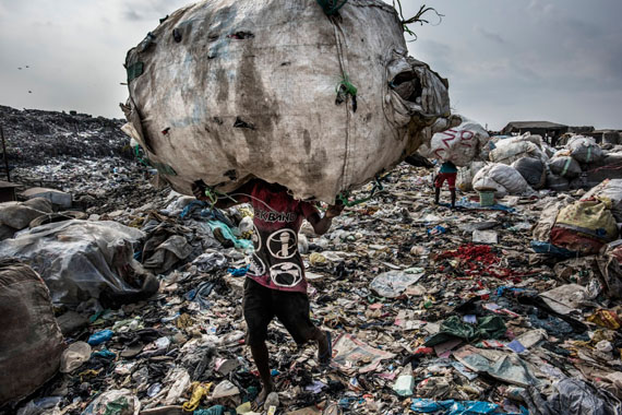 Kadir van Lohuizen / NOOR, Nigeria, Lagos, 27 January 2017 A man carries a huge back of pet bottles collected for recycling at the Olusosun landfill. The Olusosun landfill in Lagos receives between 3-5000 tons per day and is about 45 ha in size. About 5000 scavengers work here and often also live. They collect anything that is recyable like plastics, textiles, electronics, paper etc. The problem is that the landfill is full and the city wants to close it down. The question is where it will go, there are no incinerators and the infrastructure to formally recycle is lacking. There is one other landfill, but it needs to close as well. Remarkable is that the landfills in Lagos smell less compared to other landfills in the world: Nigerians throw away less food, because they either finish their plate or feed it to the animals.  