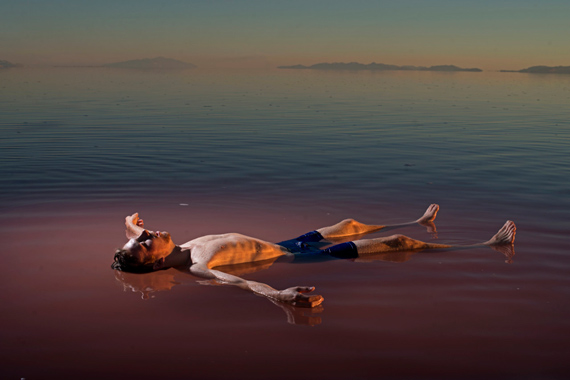 Carolyn Drake USA. Great Salt Lake, UT. 2016. Floating on north shore of the great salt lake near the Spiral Jetty. Benjamin Anderson, a student. In 1959, a 30-foot stone railroad causeway replaced the battered wood trestle. As a result, lake circulation reduced drastically. Great Salt Lake now has two distinct sections, the north arm and the south arm. The water in the north arm has a high salt concentration of approximately 26–28% due to little freshwater input. Only two types of known bacteria can currently live in the saturated North Arm waters: the halophiles Halobacterium and Halococcus. A purplish pigment in these halophiles is responsible for the unique reddish color of GSL's northern section. © Carolyn Drake | Magnum Photos