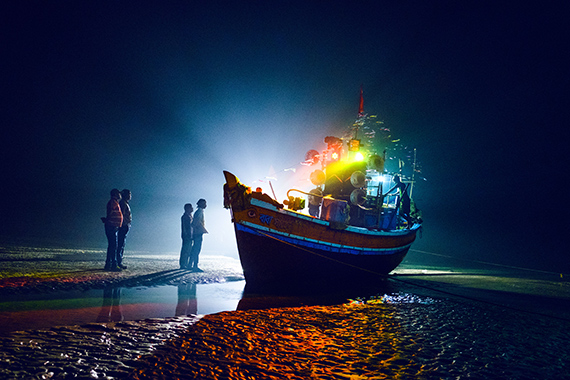 Boats bedecked with lights returning from a pilgrimage wait in the shoals for the tide to return so that they can head back home to their village. 2019 ©  Arko Datto