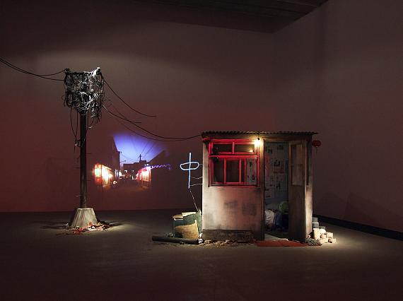 Tracey Snelling: Wang's House, 2009wood, paint, newspaper, posters, electroluminescent wire, lights, garbage, furniture, tv, telephone pole, wires, food, projector197 x 203 x 344 cm, House : 197 x 203 x 203 cm, Telephone Pole: 344 x 80 x 50 cm